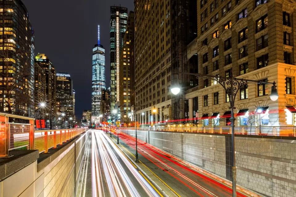 Blurred traffic at night passing through Battery Park Tunnel into New York City with One World Trade Center in background.